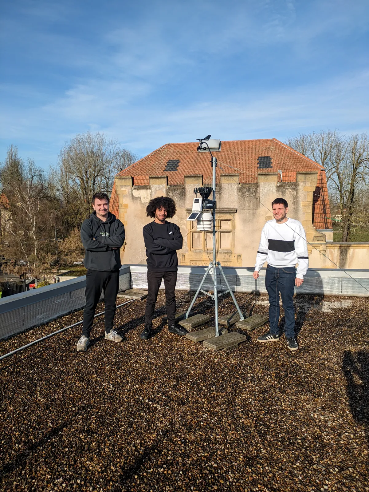 Trois personnes sur un toit, autour d’une station météo connectée